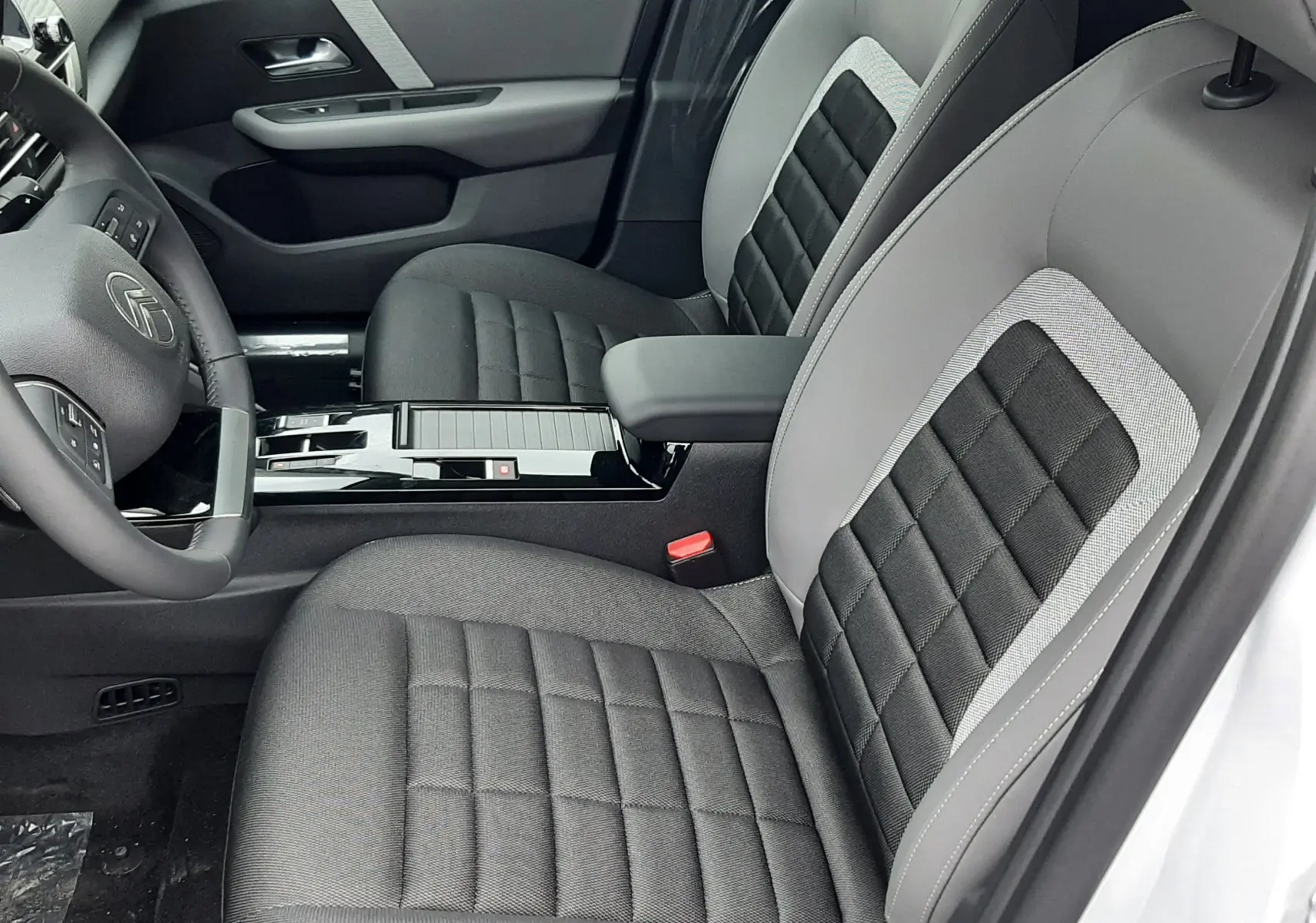 Intérieur avant droit d'une Citroën C4 2025 hybride, sièges gris à inserts noirs et console centrale brillante noire.
