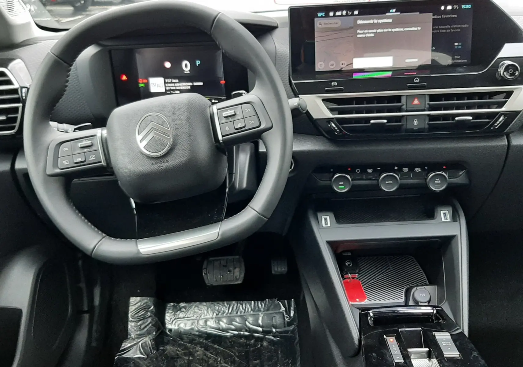 Vue intérieure du poste de conduite de la Citroën C4 hybride 2025 avec volant multifonction et écran tactile central.