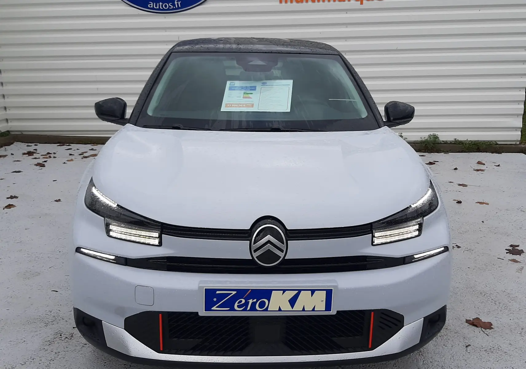 Vue frontale d'une Citroën C4 2025 blanc Okenite avec toit noir Perla, feux LED et plaque Zéro KM visible.