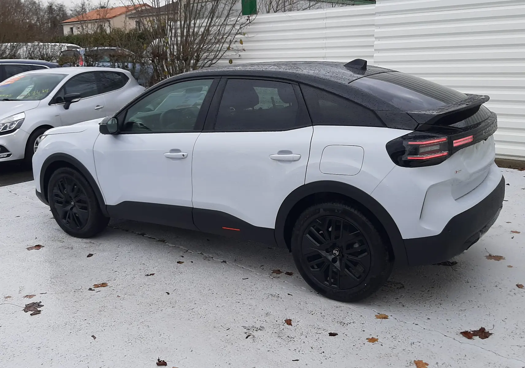 Vue côté gauche arrière d'une Citroën C4 hybride blanche avec toit noir et jantes noires, stationnée sur sol clair.