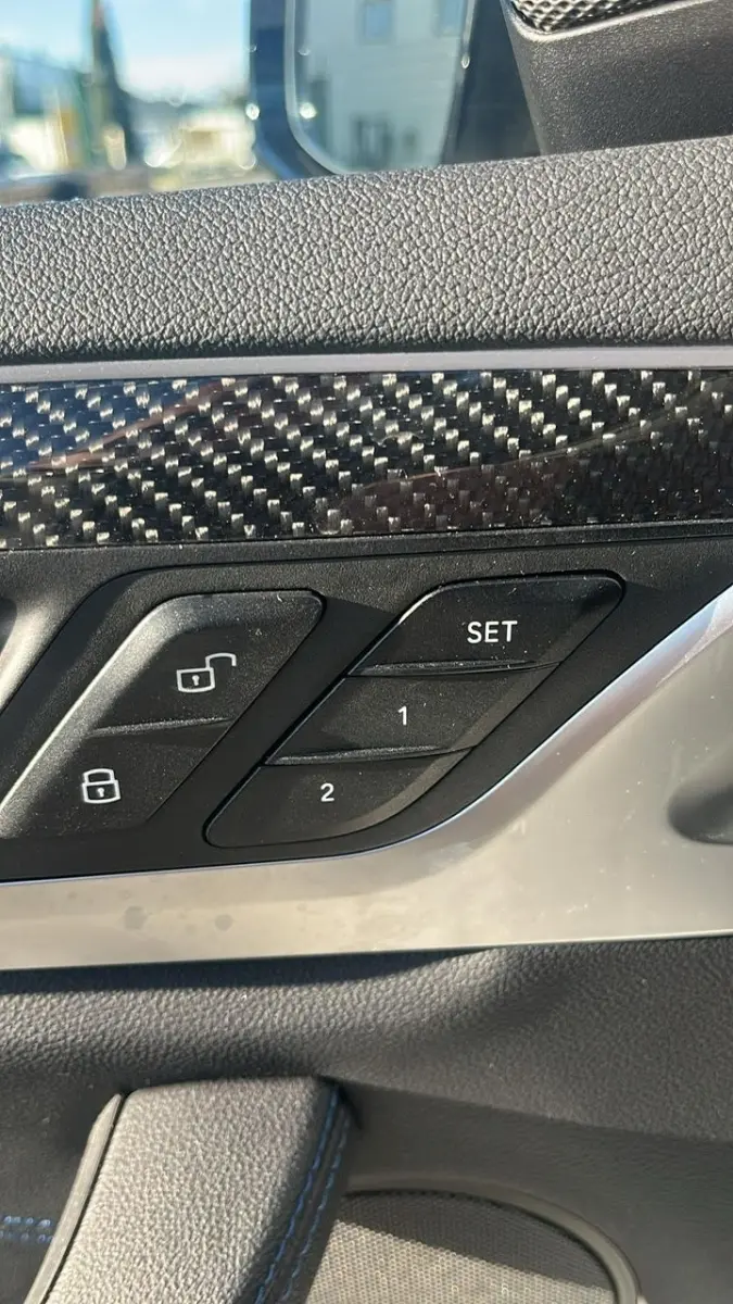 Détail intérieur côté gauche de la porte BMW X3 blanc, boutons de verrouillage et mémoire sièges avec finition carbone.