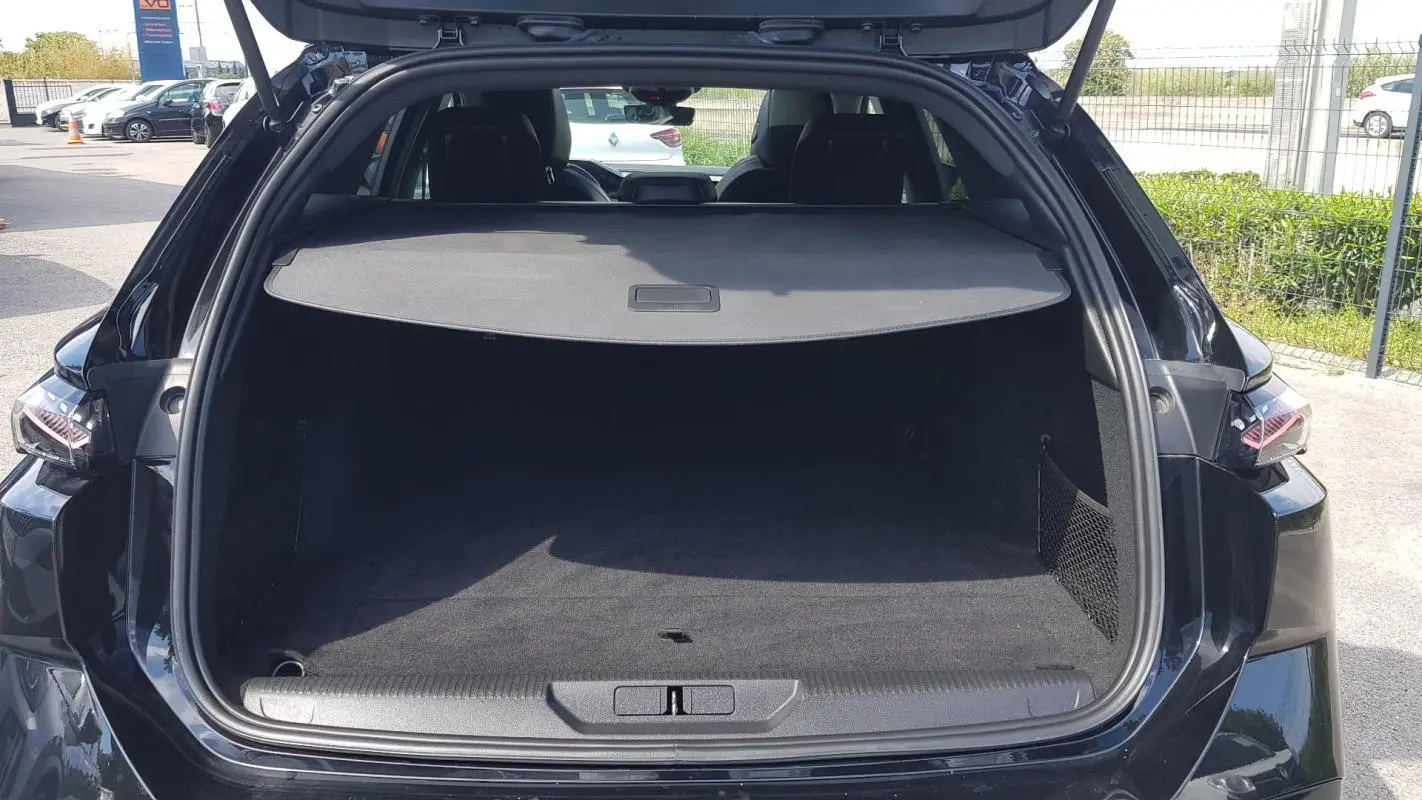 Vue arrière ouverte du coffre noir du Peugeot 308 SW PHEV 225 e-EAT8 GT avec cache-bagages et filet latéral.