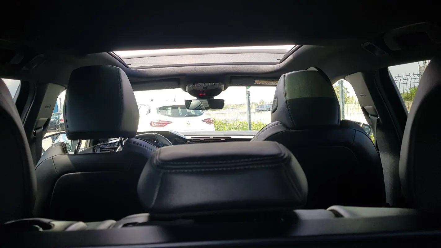 Vue intérieure arrière de la Peugeot 308 SW PHEV 225 e-EAT8 GT noire, avec toit ouvrant électrique et sièges en cuir noir.