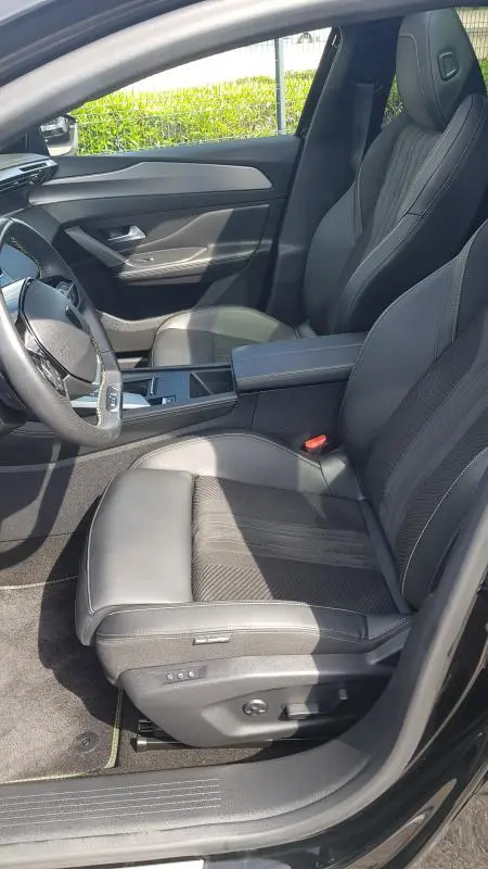 Intérieur côté conducteur de la Peugeot 308 SW PHEV 225 e-EAT8 GT 2023, sièges cuir noirs et accoudoir central visible.