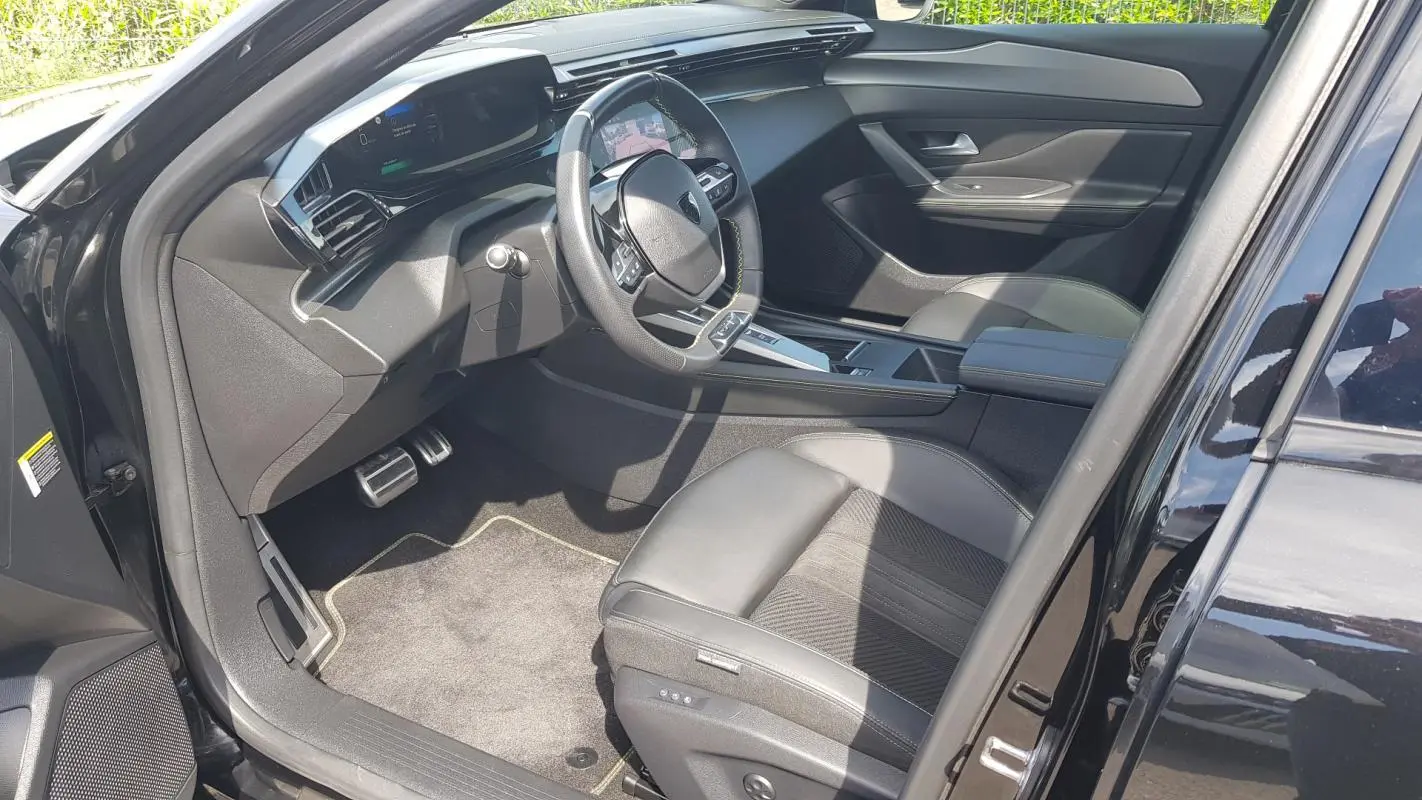 Intérieur avant droit de la Peugeot 308 SW PHEV 225 GT 2023 noir, volant cuir et cockpit numérique visible.