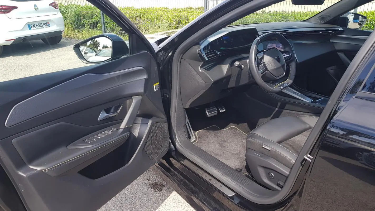 Intérieur côté conducteur de la Peugeot 308 SW PHEV noire 2023, montrant siège, volant cuir et tableau de bord numérique.