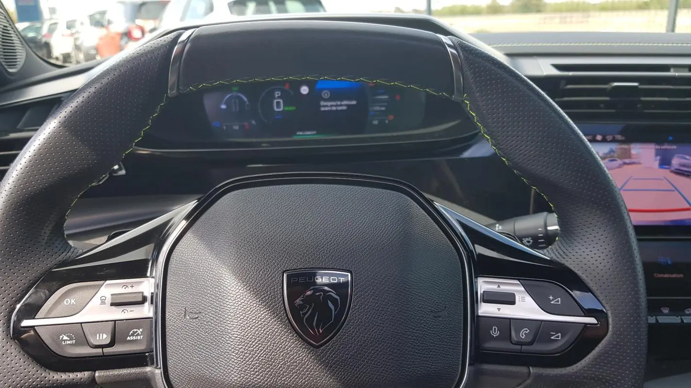 Vue rapprochée du volant cuir noir perforé de la Peugeot 308 SW PHEV 225 e-EAT8 GT avec tableau de bord numérique.