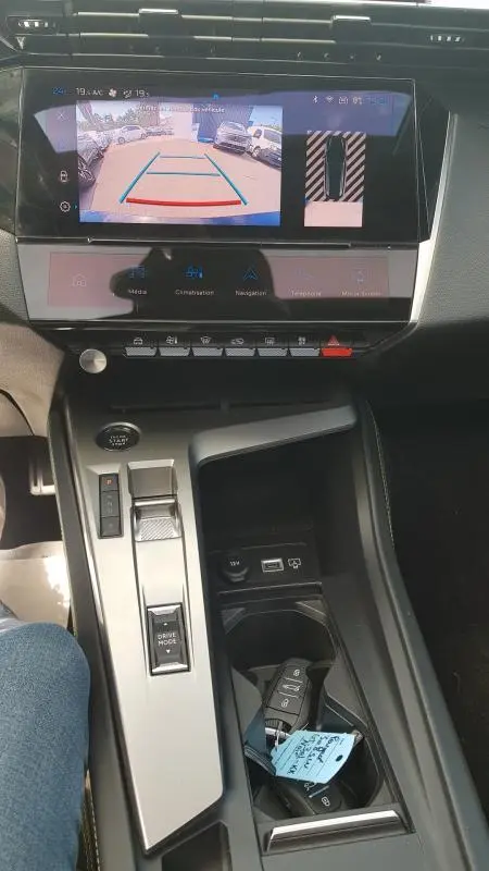 Vue intérieure centrée sur la console centrale et l'écran tactile affichant la caméra de recul du Peugeot 308 SW noir PHEV 2023.
