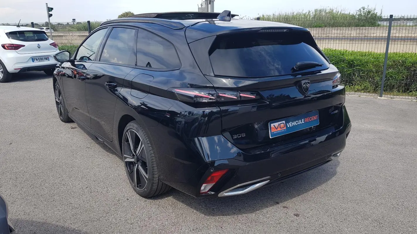 Peugeot 308 SW PHEV noir vue 3/4 arrière droit, avec jantes alliage 18 pouces et barres de toit visibles.