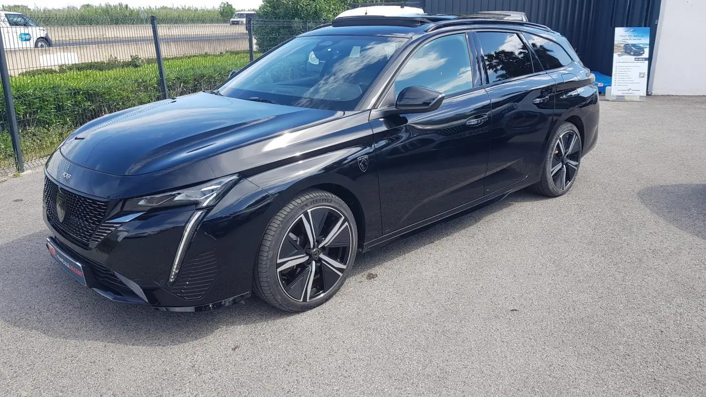 Peugeot 308 SW PHEV noir en 3/4 avant droit, avec jantes alliage 18 pouces et barres de toit visibles.