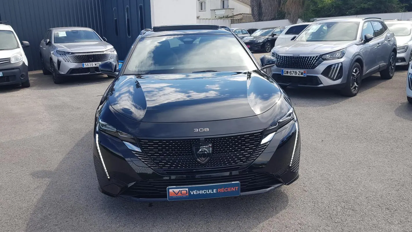 Peugeot 308 SW PHEV noir vue de face, avec calandre noire et feux LED verticaux allumés.
