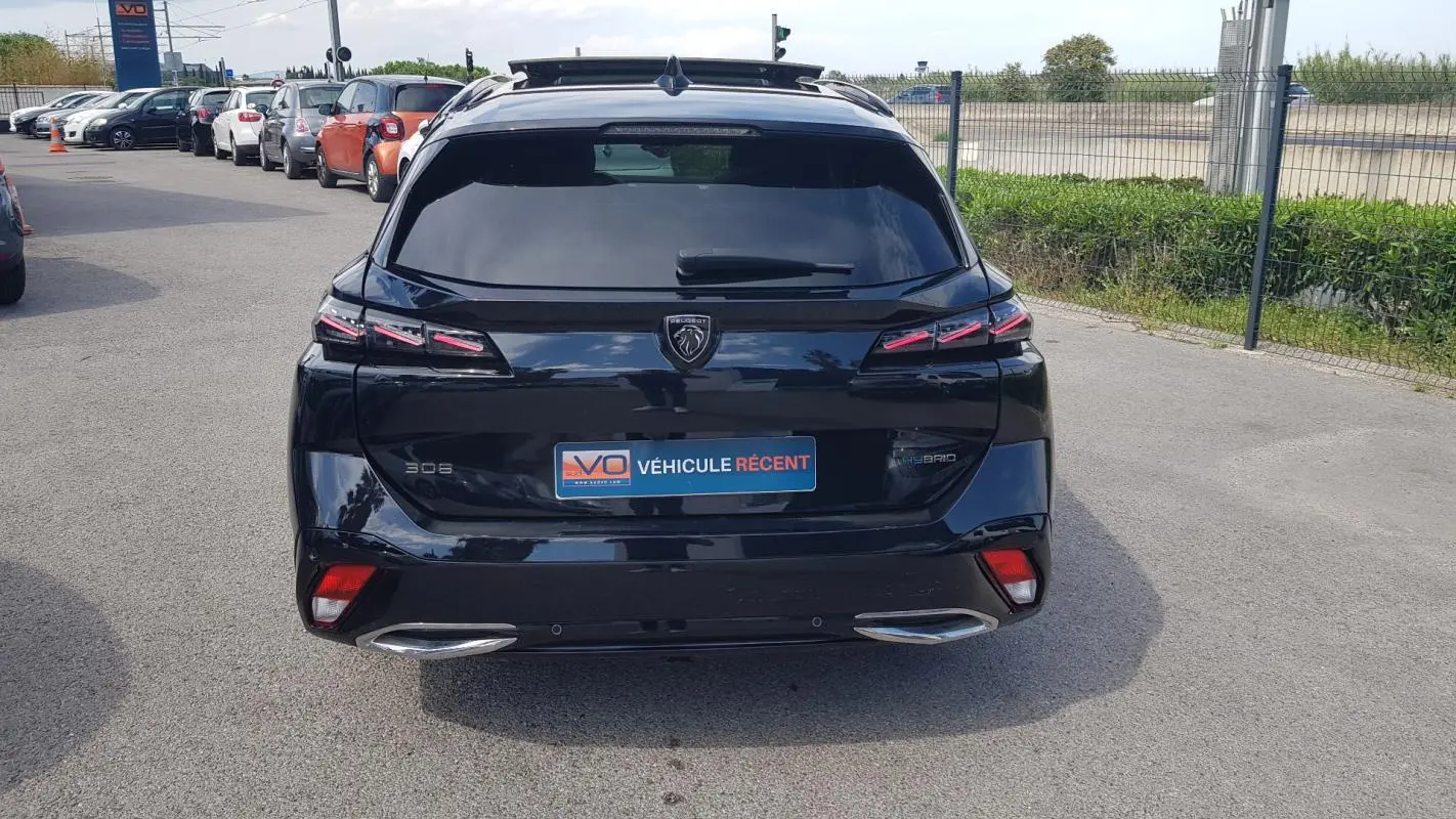 Vue arrière d’une Peugeot 308 SW PHEV 225 e-EAT8 GT noire avec feux LED et double sortie d’échappement chromée.