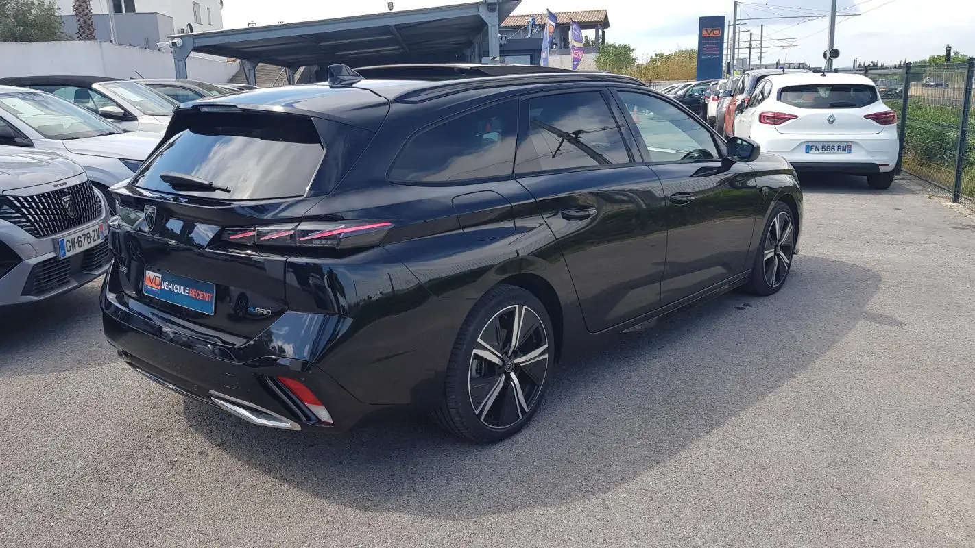 Peugeot 308 SW PHEV noir en 3/4 arrière droit, avec jantes alliage 18 pouces et barres de toit visibles.