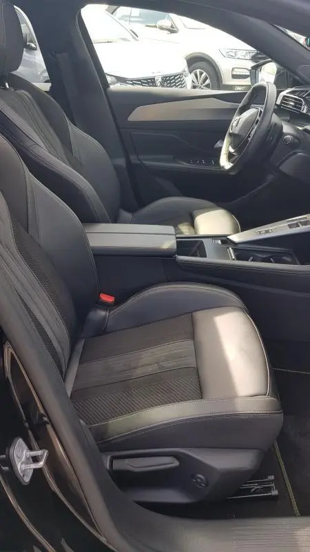 Intérieur avant droit de la Peugeot 308 SW PHEV 225 GT 2023 noire, sièges cuir avec accoudoir central et volant cuir.