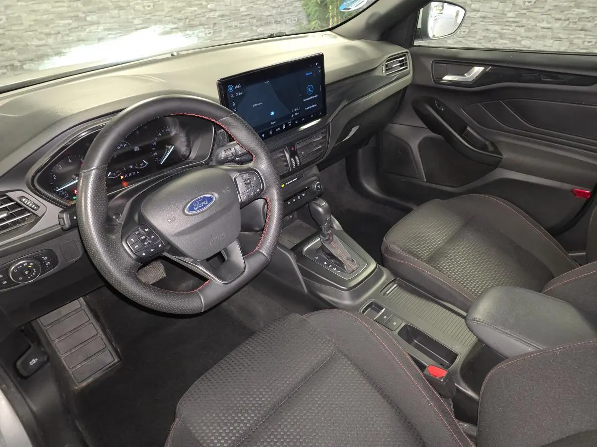 Vue intérieure côté conducteur de la Ford Focus 2024 gris, volant ST à surpiqûres rouges et écran tactile central.