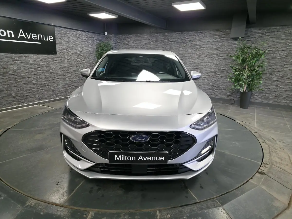 Vue avant d'une Ford Focus gris métallisé avec calandre noire et badge ST-Line visible en intérieur showroom.