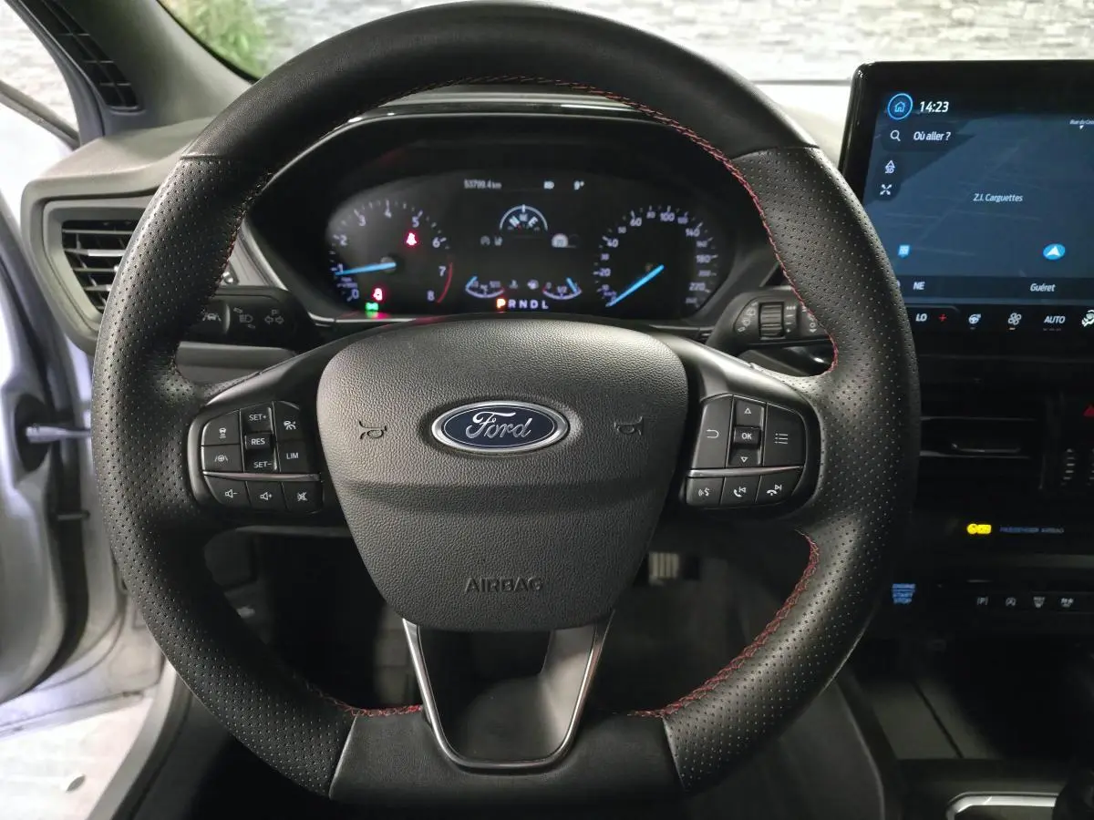 Vue intérieure centrée sur le volant perforé noir avec surpiqûres rouges de la Ford Focus 2024 gris lunaire.