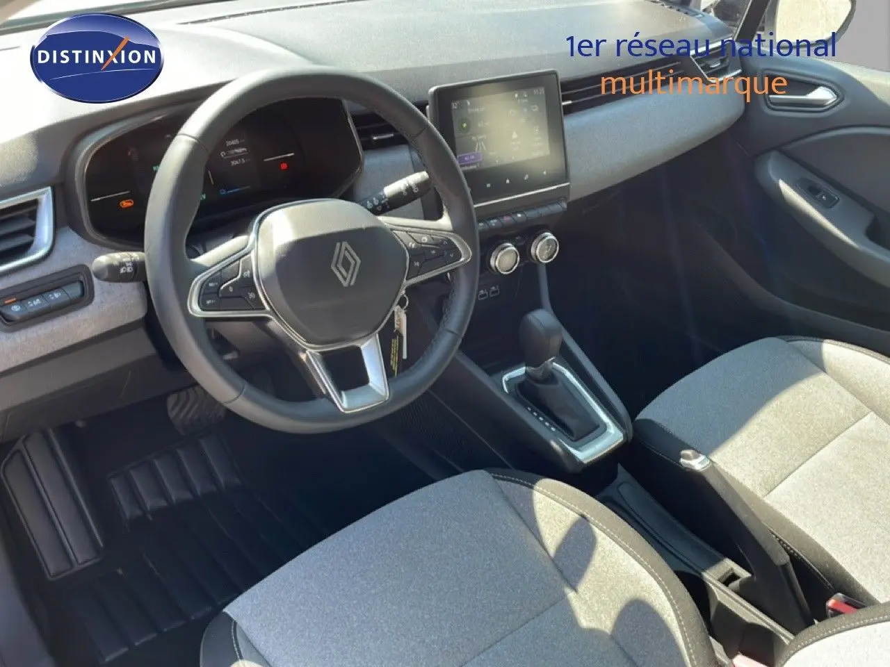 Vue intérieure de la Renault Clio 2025, tableau de bord et volant multifonction avec sellerie tissu gris clair.