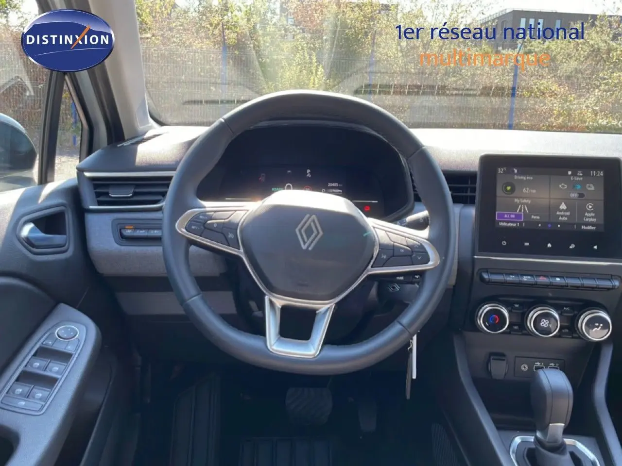 Vue intérieure centrée sur le volant Renault de la Clio blanche, avec tableau de bord numérique et écran tactile visible.