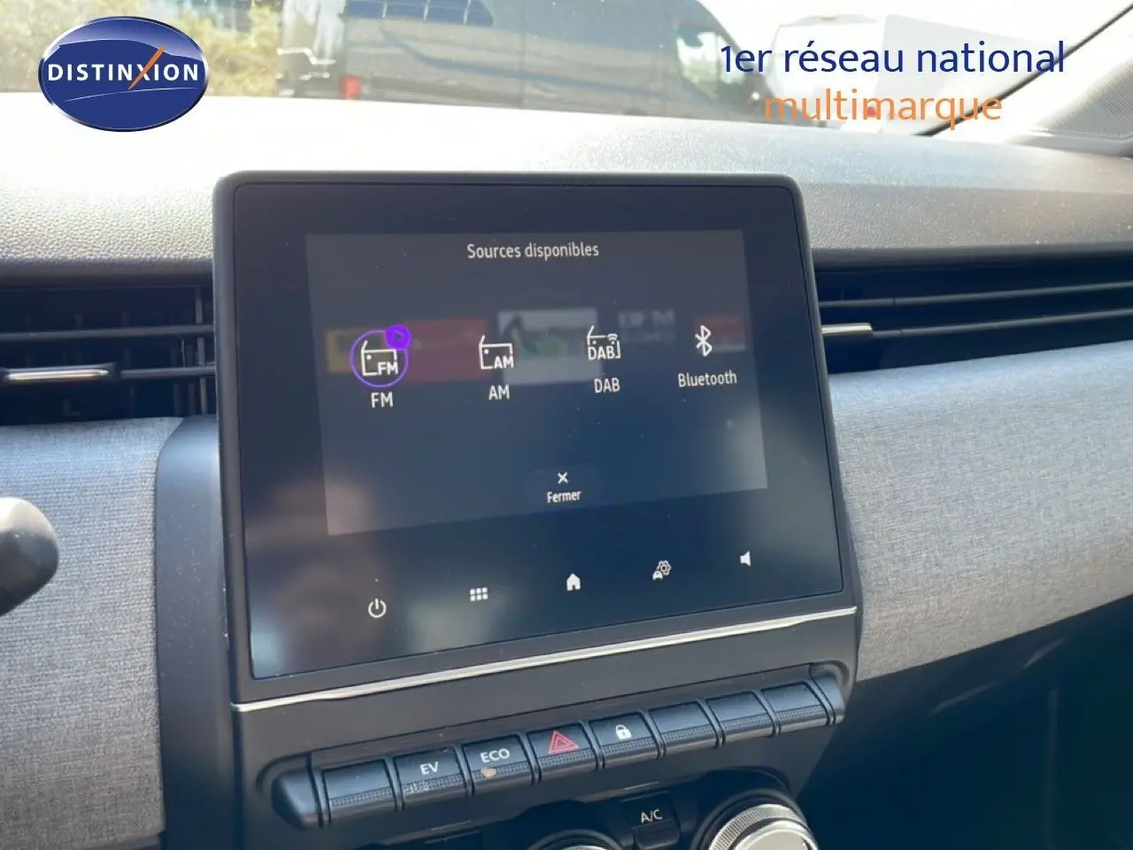 Vue intérieure centrée sur l'écran tactile multimédia de la Renault Clio blanche Glacier, avec commandes climatisation et mode EV visibles.