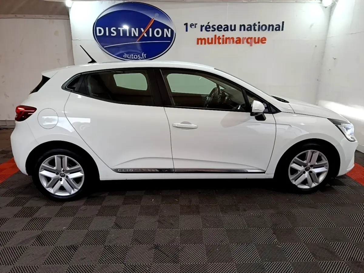 Profil droit d'une Renault Clio Business Blue dCi 85 blanche, avec jantes alliage et logo Distinxion en arrière-plan.