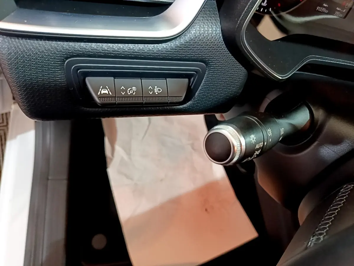 Gros plan sur les commandes d'assistance et éclairage côté gauche du tableau de bord noir d'une Renault Clio blanche 2020.