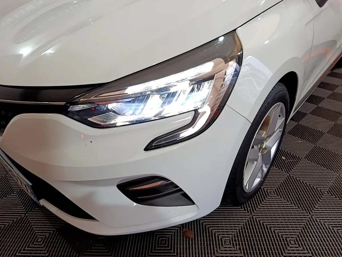 Gros plan sur l'avant droit blanc d'une Renault Clio 2020 avec phare LED allumé et jante alliage visible.