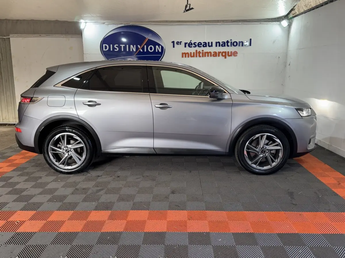 Vue de profil côté gauche d'un DS7 Crossback E-TENSE gris foncé dans un showroom avec sol à damier noir et orange.