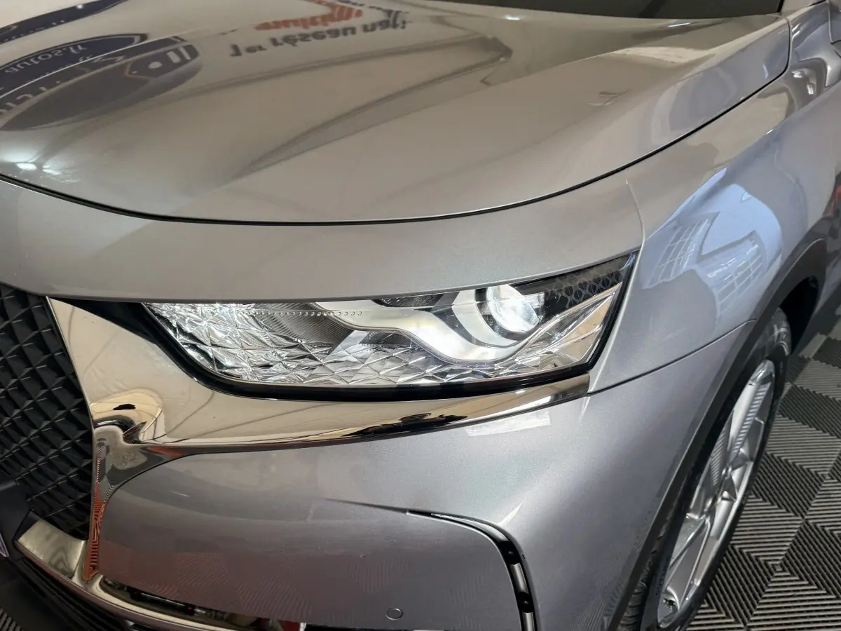 Gros plan sur le phare avant droit du DS7 Crossback E-TENSE gris foncé, mettant en valeur la calandre et la jante alu.
