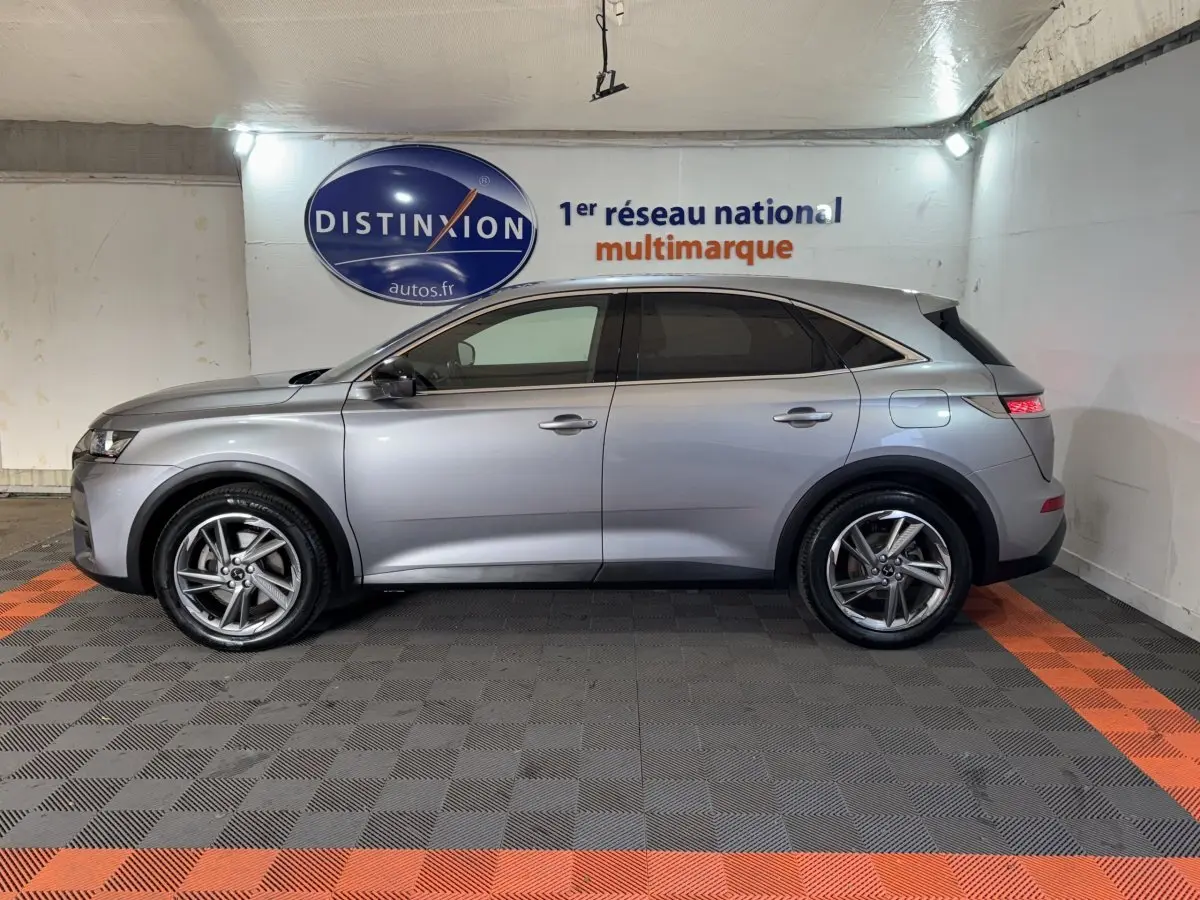 Vue de profil côté gauche du DS7 Crossback E-TENSE gris foncé dans un showroom avec sol à damier noir et orange.