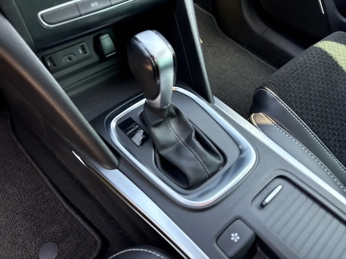 Gros plan sur la console centrale noire de la Renault Mégane avec levier de vitesse automatique et sellerie tissu noire.