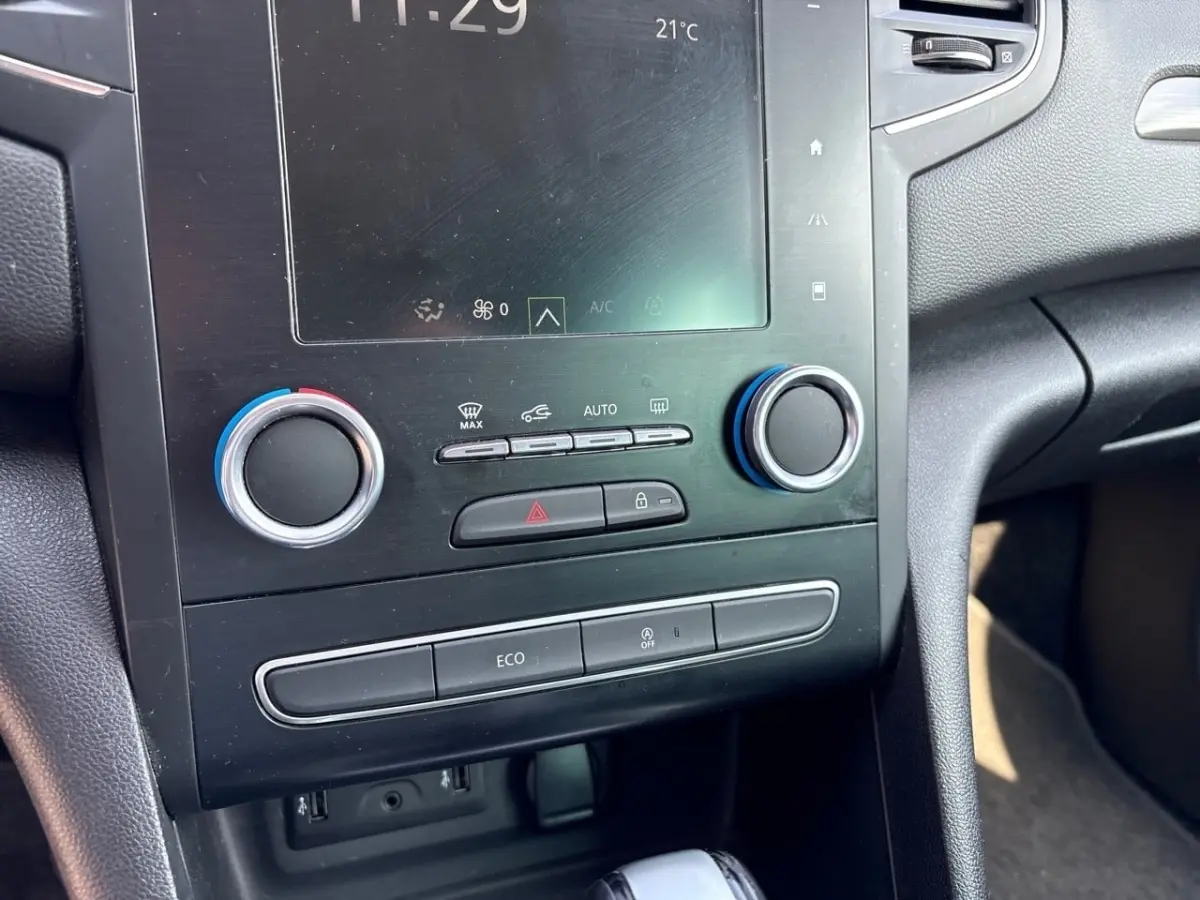 Vue rapprochée du tableau de bord central noir de la Renault Mégane Intens avec commandes climatisation et écran tactile.