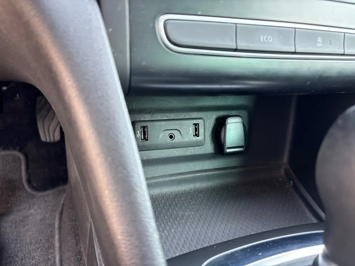 Vue rapprochée de la console centrale noire de la Renault Mégane Intens, montrant ports USB et prise 12V.