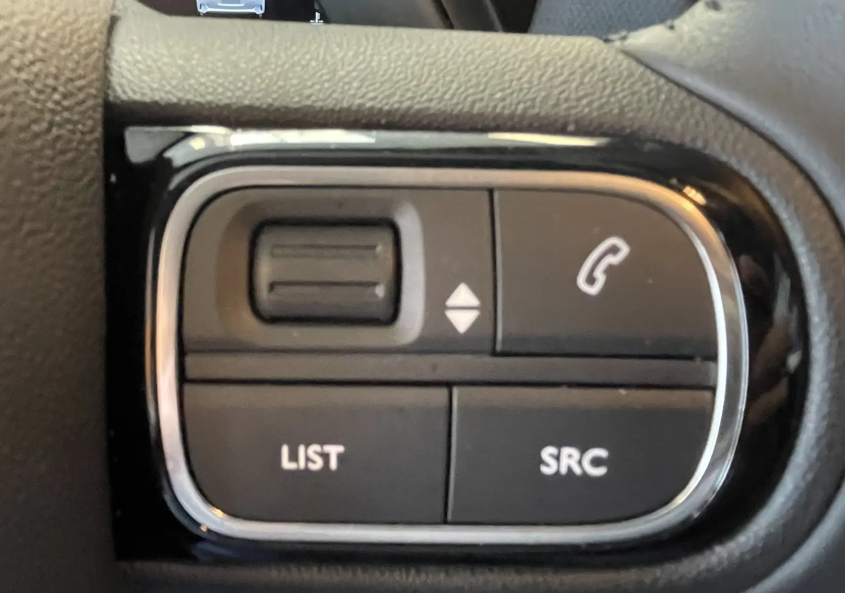 Gros plan sur les commandes au volant du Citroën C5 Aircross hybride 2025, boutons noirs avec contours chromés.