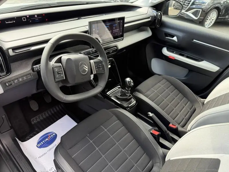Vue intérieure côté conducteur de la Citroën C3 1.2 Turbo 2025 avec sièges tissu noir et console centrale manuelle.