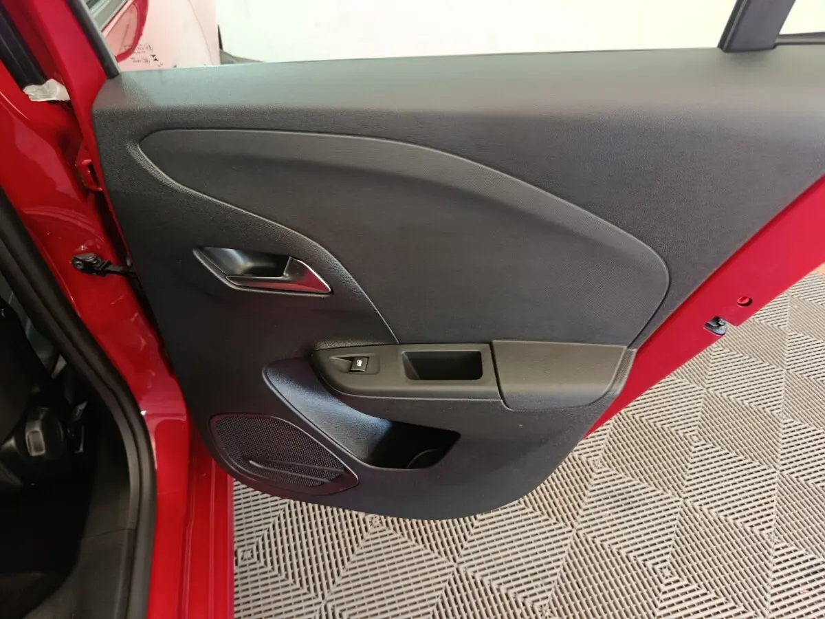 Vue rapprochée de la porte arrière gauche noire d’une Opel Corsa rouge 2023, avec poignée et commande de vitre.