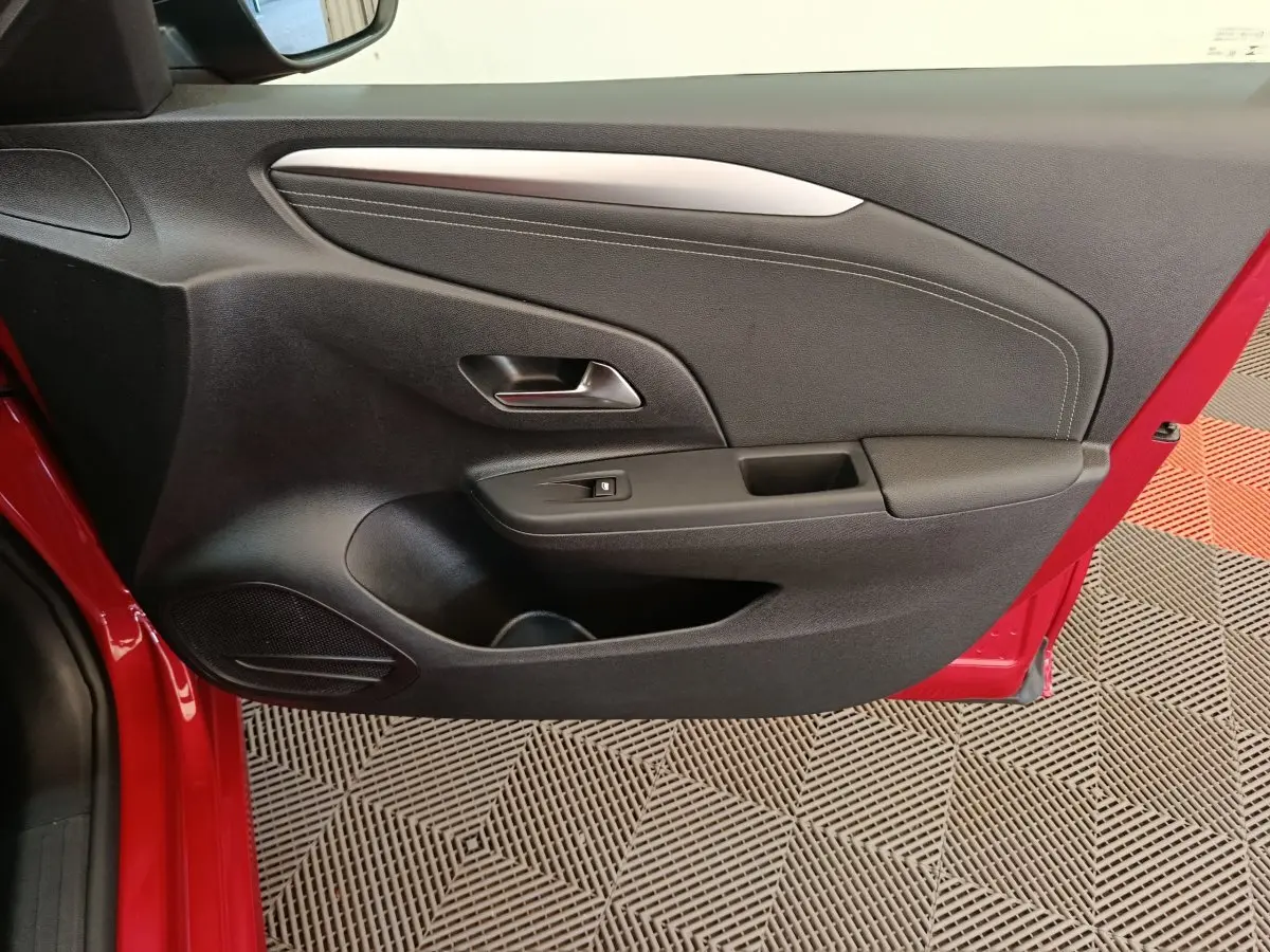 Vue rapprochée de la porte intérieure côté gauche rouge de l’Opel Corsa 1.2 Turbo 2023 avec poignée et commande de vitre.