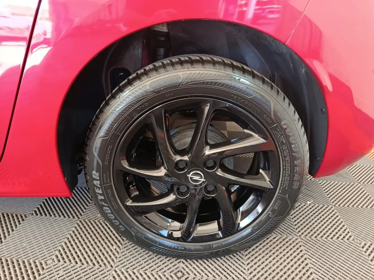 Gros plan sur la roue avant droite noire brillante d’une Opel Corsa rouge 2023, avec logo Opel au centre.