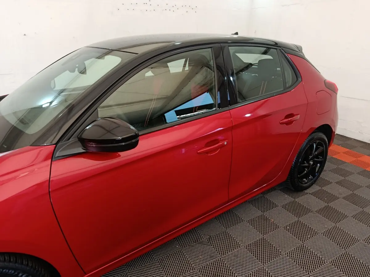 Vue latérale droite d'une Opel Corsa rouge 2023 avec toit noir et jantes noires brillantes.