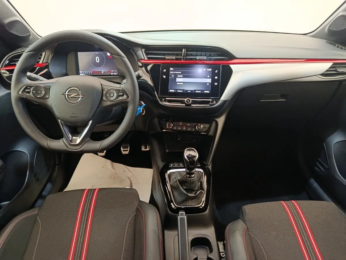 Vue intérieure avant de l’Opel Corsa rouge 2023, volant multifonctions, écran tactile central et levier de vitesse manuel.