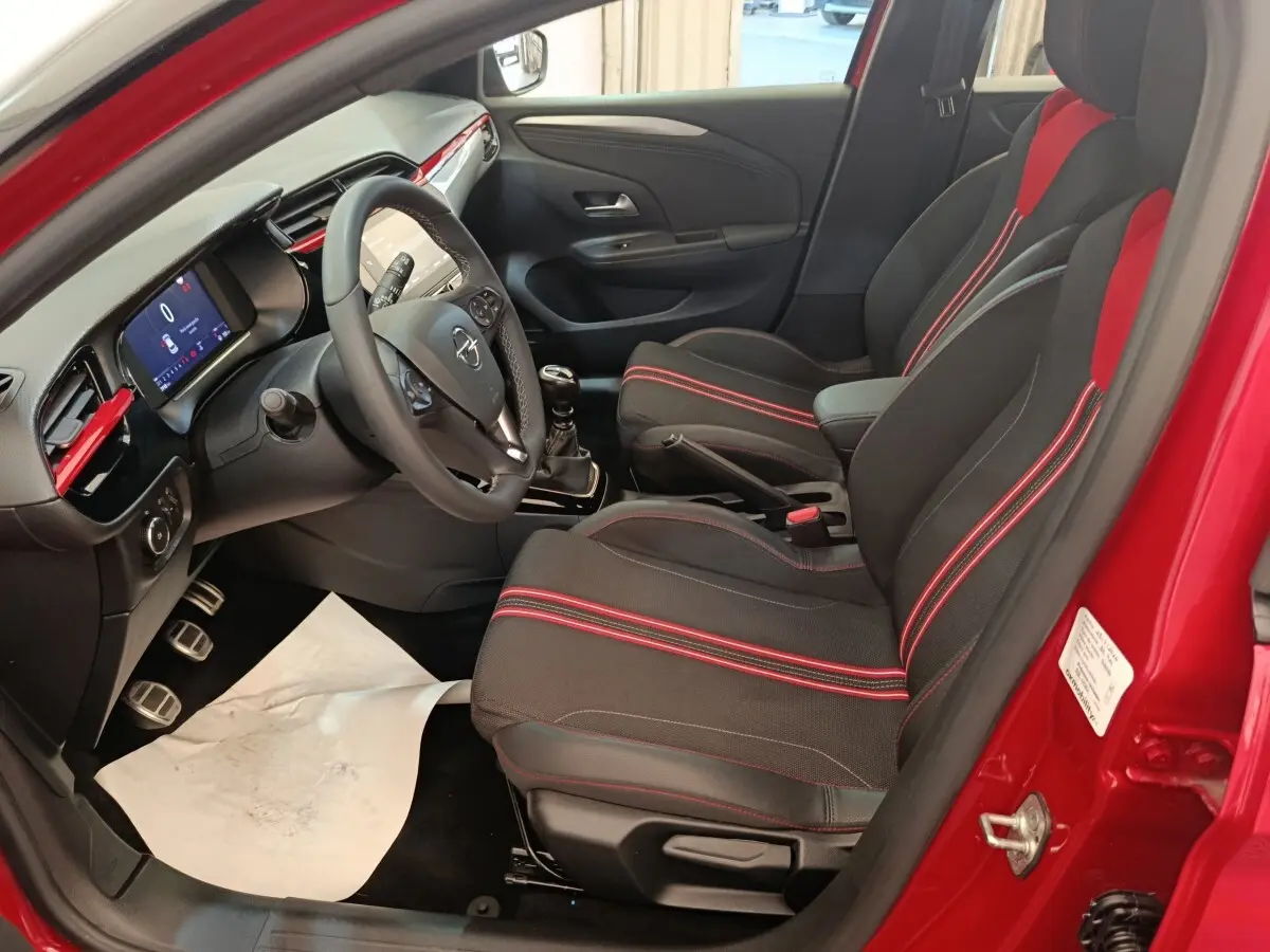 Intérieur de l’Opel Corsa rouge 2023, vue côté conducteur, sièges noirs avec surpiqûres rouges et tableau de bord digital.