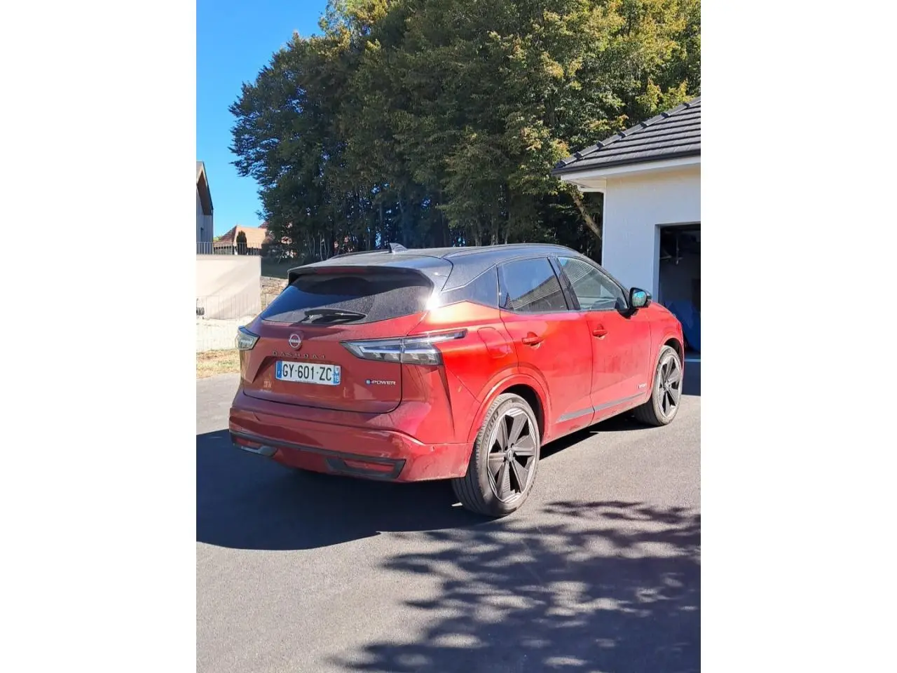 Vue 3/4 arrière droite d'un Nissan Qashqai 1.5 e-Power Tekna rouge foncé avec toit noir et jantes noires.