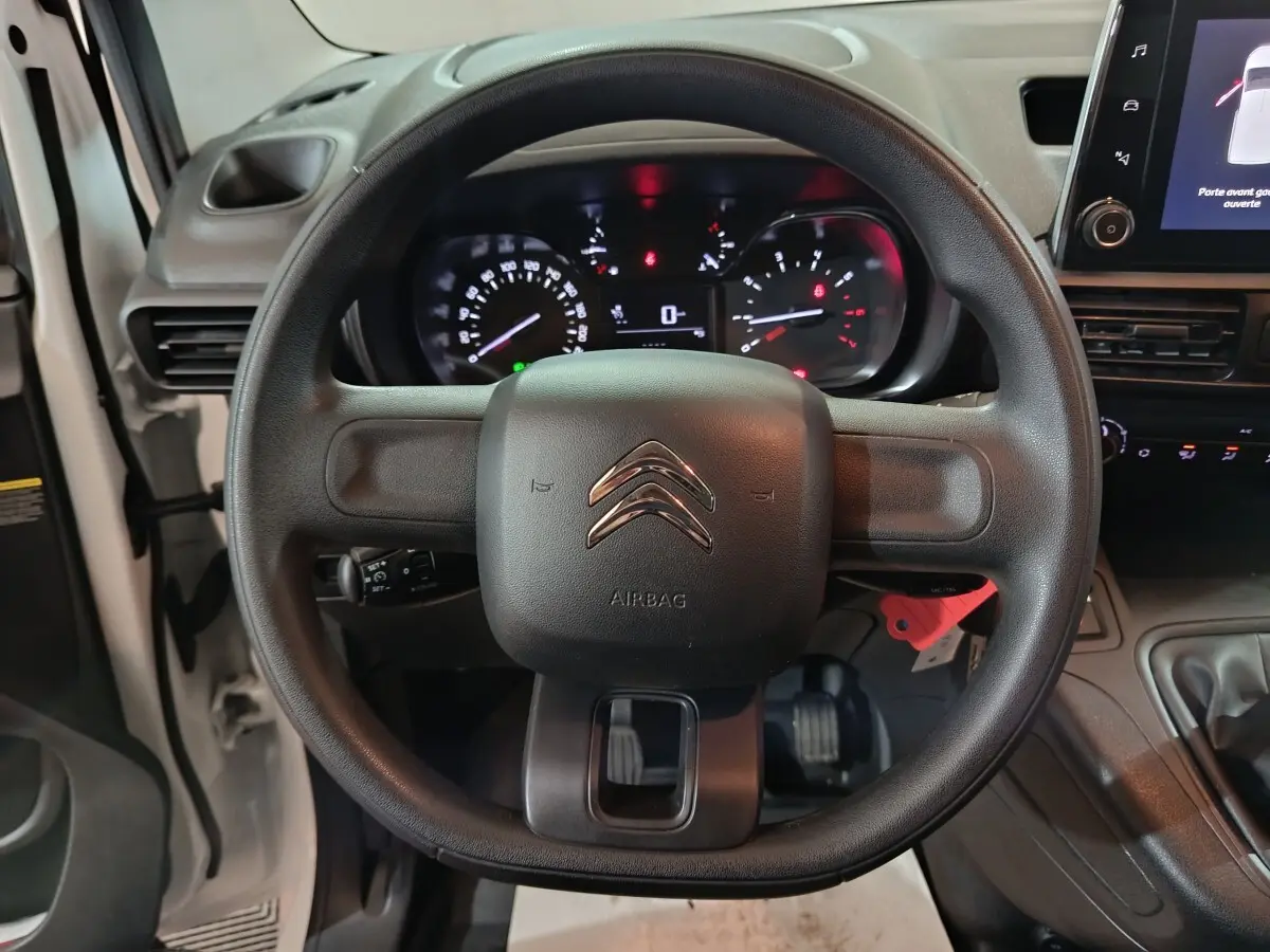 Vue rapprochée du volant noir de la Citroën Berlingo blanc, avec tableau de bord et écran tactile visibles.