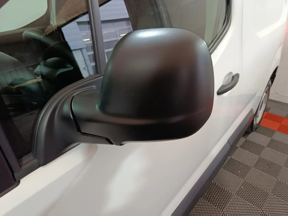 Gros plan sur le rétroviseur noir côté gauche du Citroën Berlingo blanc, avec partie de la porte visible.