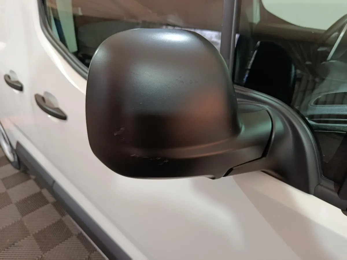 Gros plan sur le rétroviseur noir côté gauche d’un Citroën Berlingo blanc, vue latérale avant.