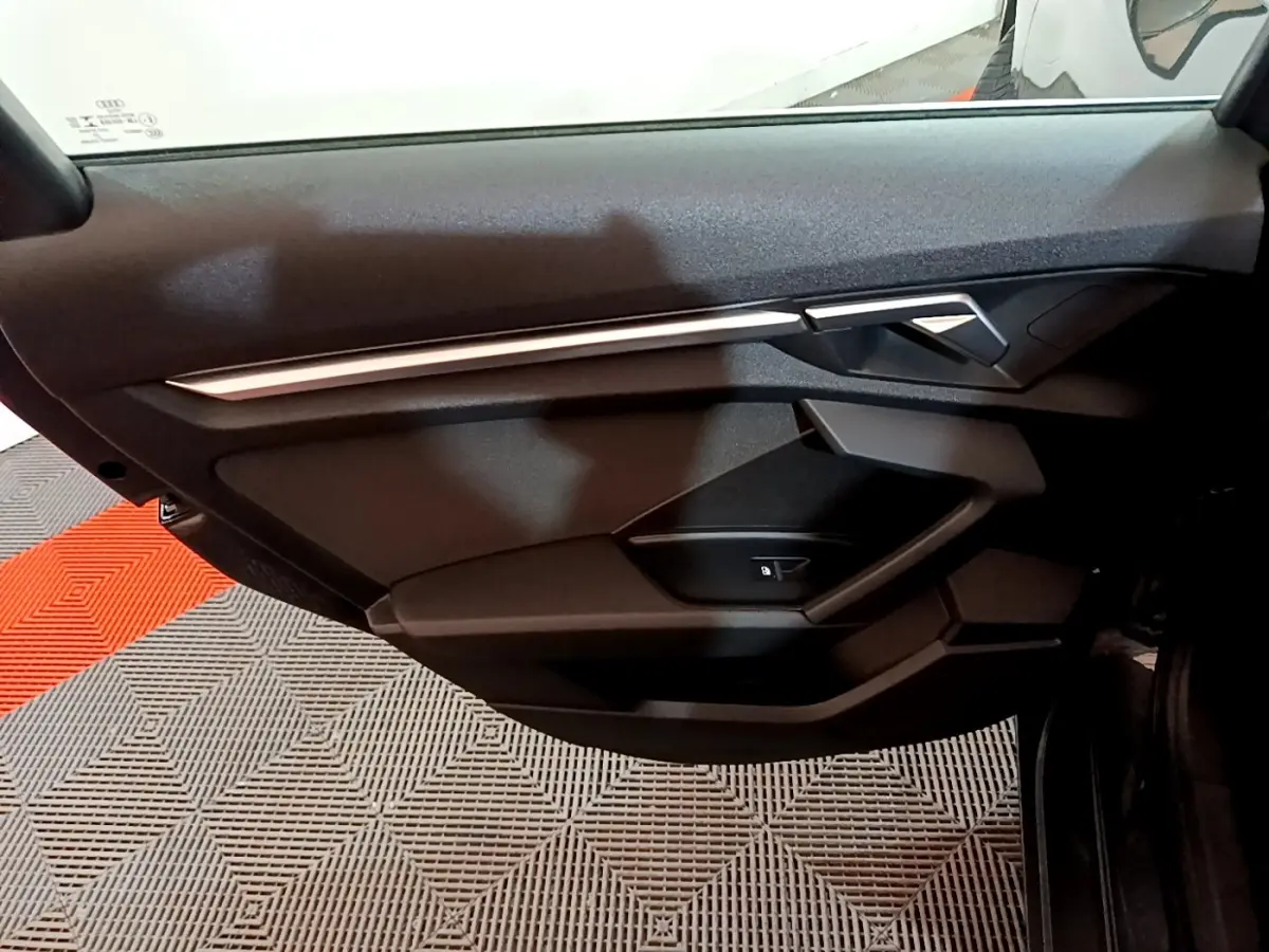 Vue intérieure du panneau de porte côté gauche de l'Audi A3 gris foncé, avec poignée et commande de verrouillage.