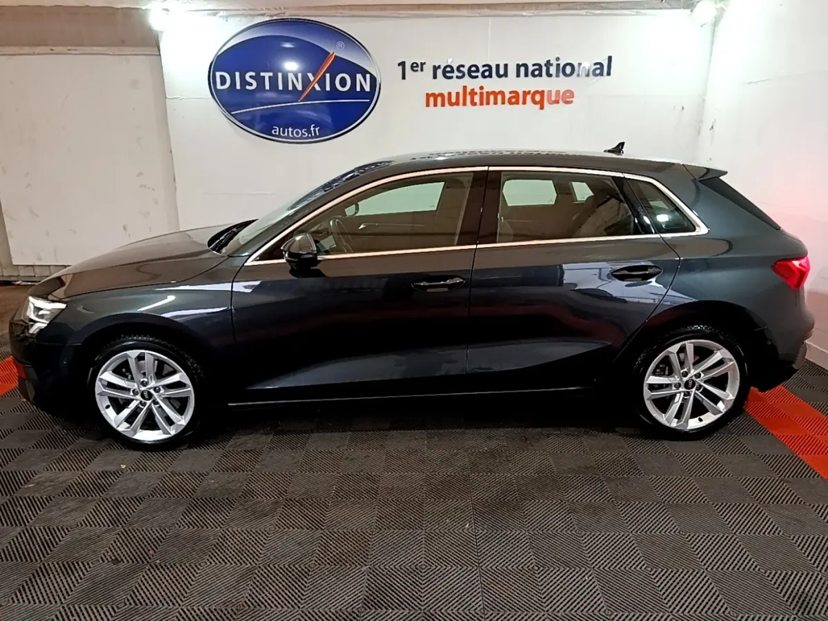 Audi A3 gris foncé vue de profil côté gauche, avec jantes alliage et toit ouvrant en intérieur showroom.