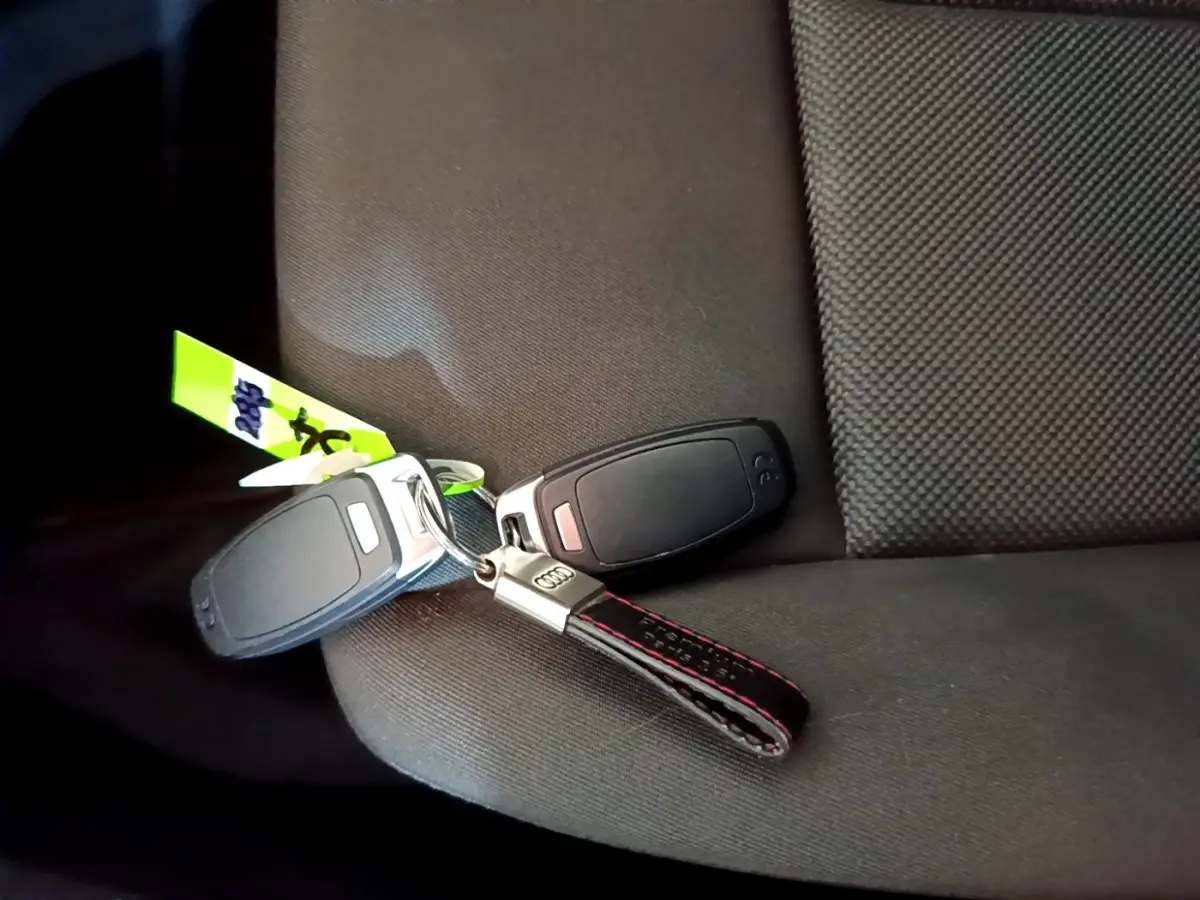 Clé Audi avec porte-clés cuir noir et surpiqûres rouges posée sur un siège tissu gris foncé.