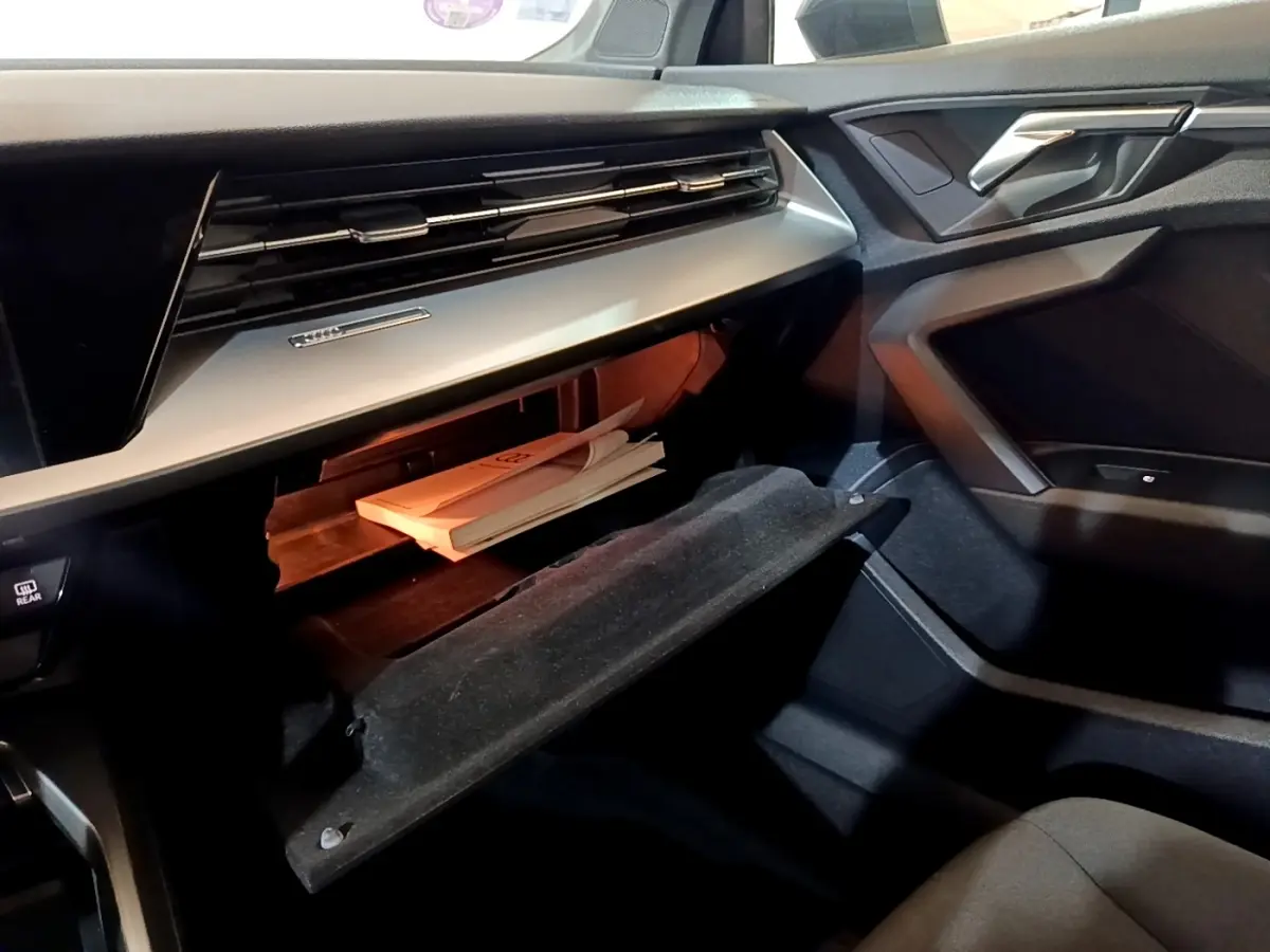 Intérieur côté passager de l'Audi A3 gris foncé 2021, boîte à gants ouverte avec documents visibles.