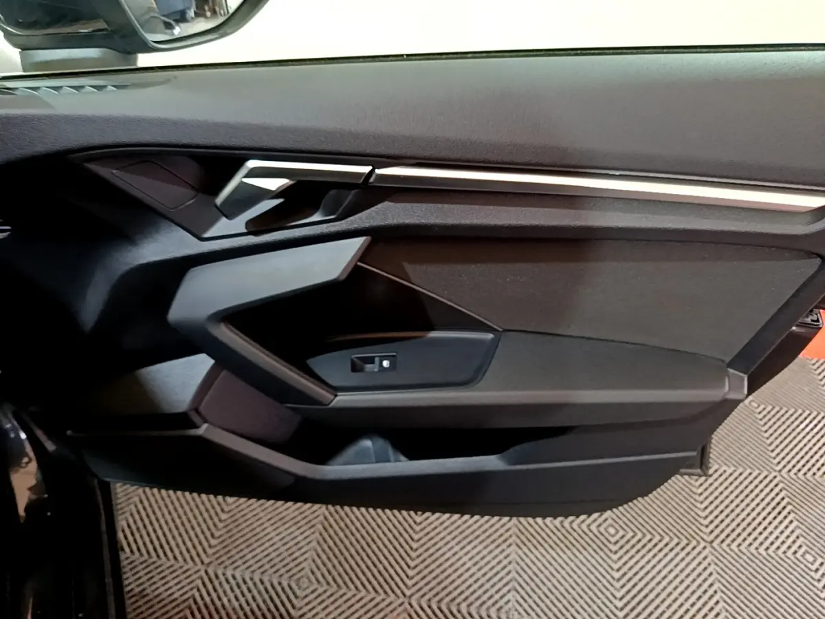 Vue rapprochée de la porte intérieure côté gauche d'une Audi A3 gris foncé, avec poignée et commande de vitre.